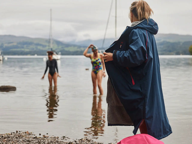 2 women paddling in the water and another woman on the shore removing her Red Pro Change Robe